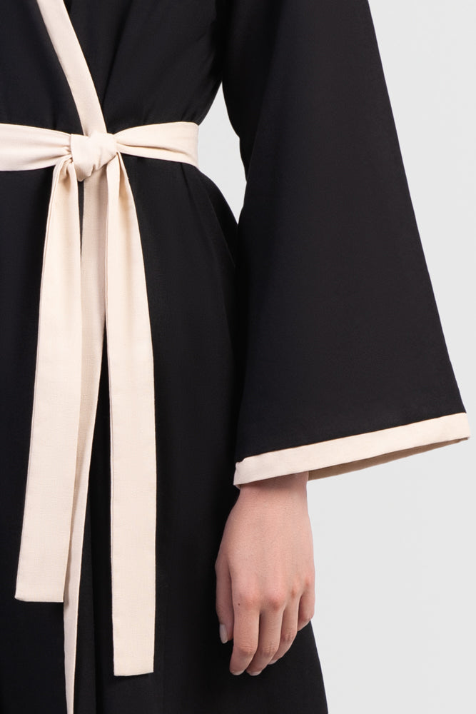 Black linen cotton kimono-style abaya with off-white trim along edges and matching belt details close-up