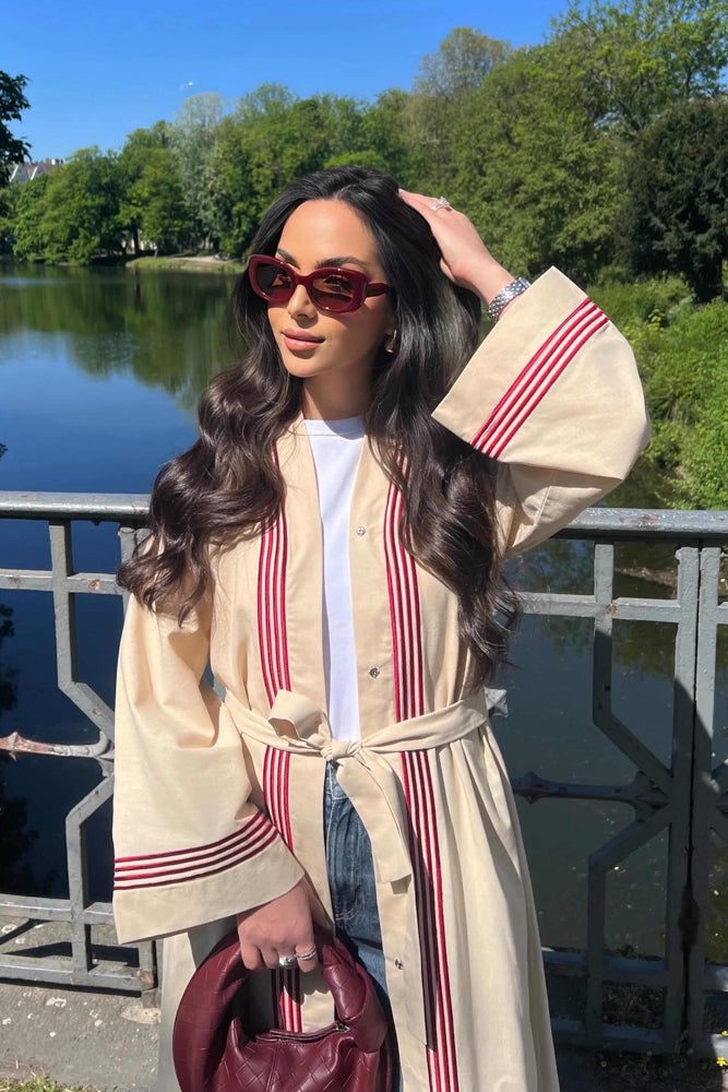 Beige linen abaya with vertical red stripes around front placket and sleeve cuffs